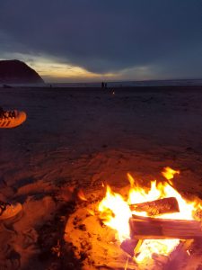 Bonfire at dusk on beach along oceanside.